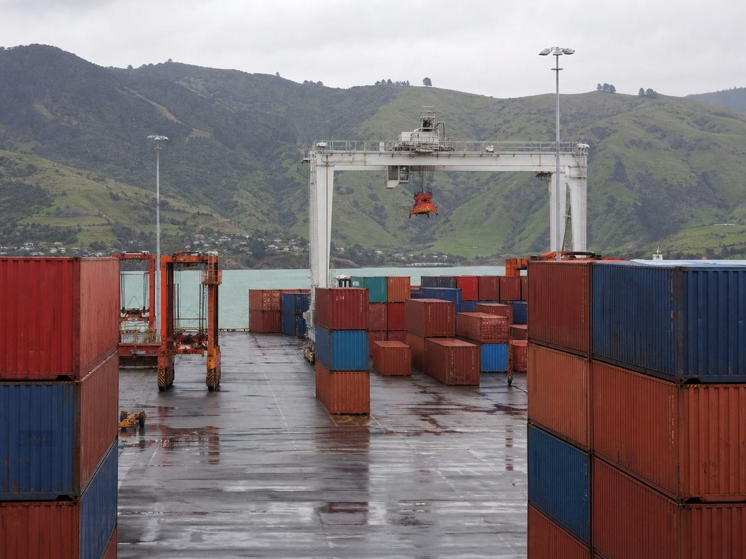 Stacked shipping containers and a gantry crane at a New Zealand port on an overcast day